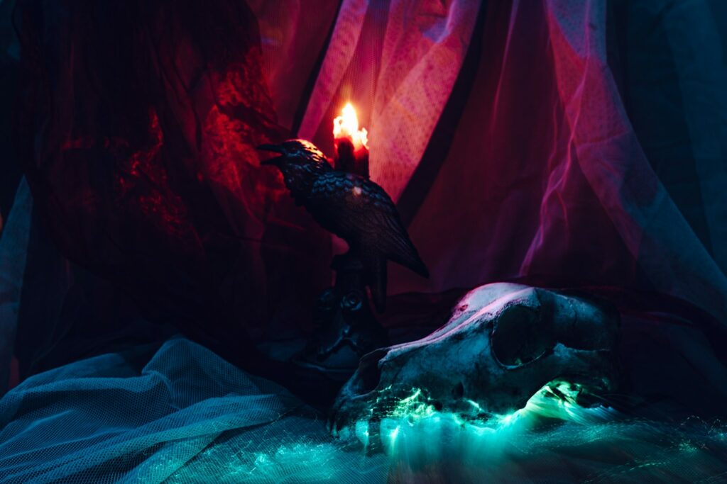 Mise en scène dark fantasy : crâne d'animal, corbeau sculpté et bougie allumée dans une lumière rouge et verte